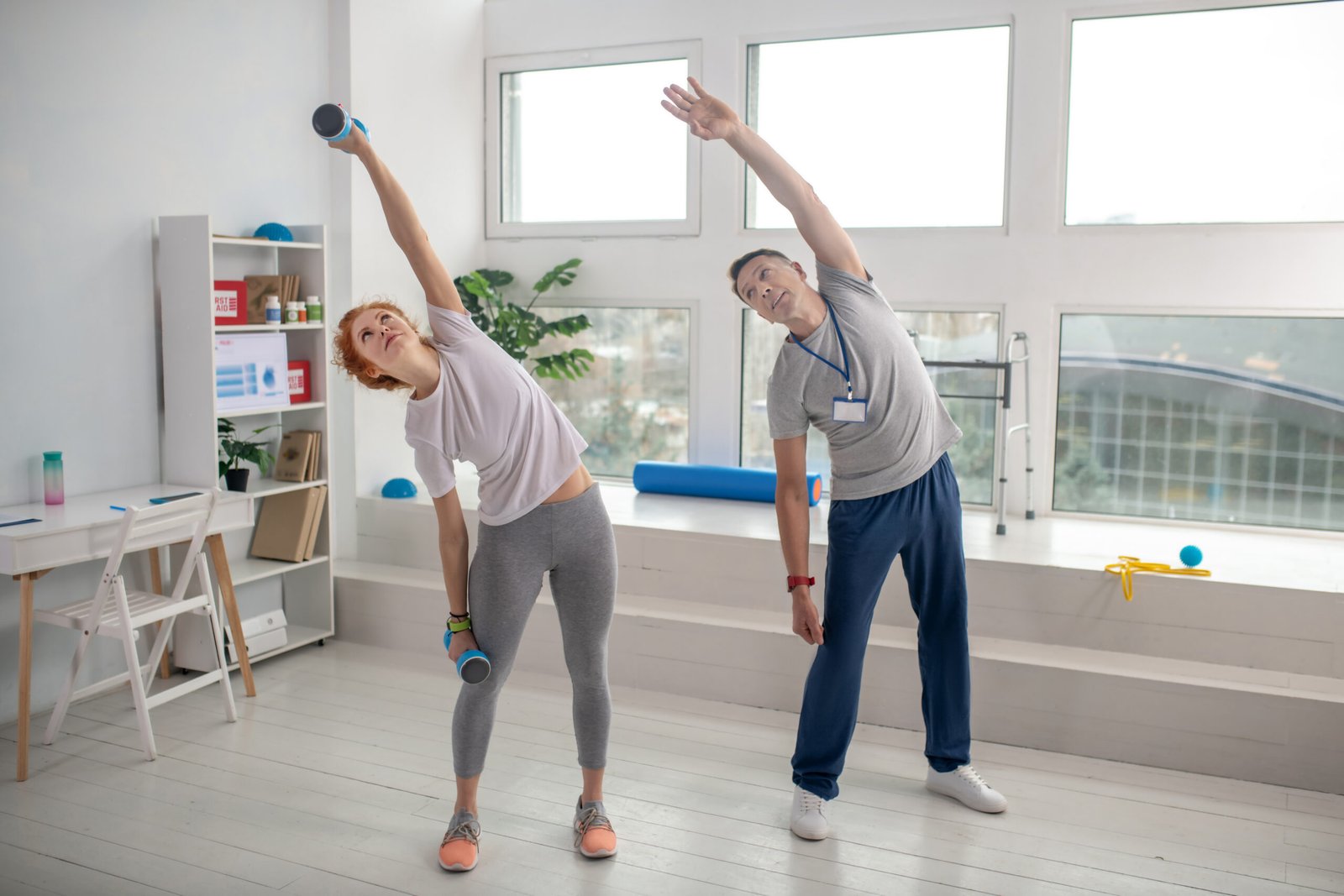 Female patient holding dumbbells and bending sideways together with male physiotherapist